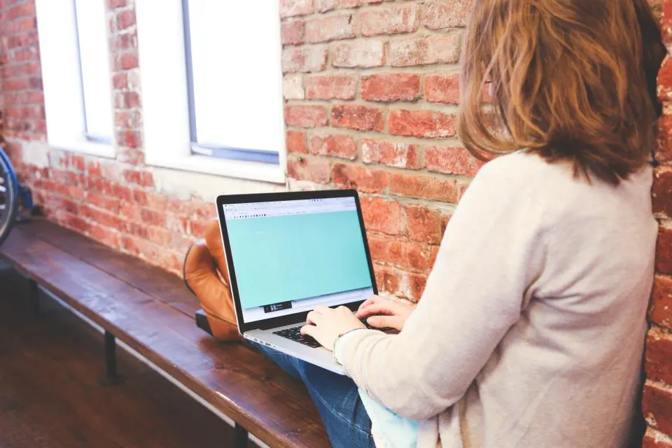 A student typing on a laptop by a window